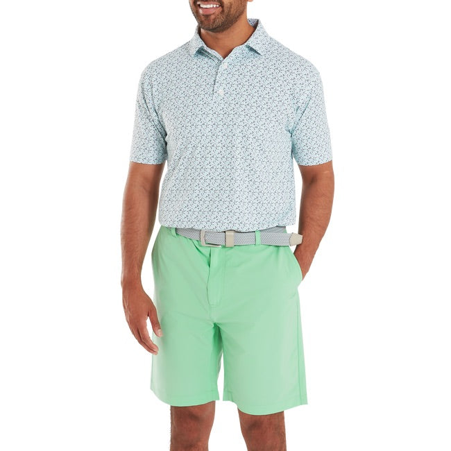 Man wearing a patterned short-sleeve shirt and light green shorts on a white background