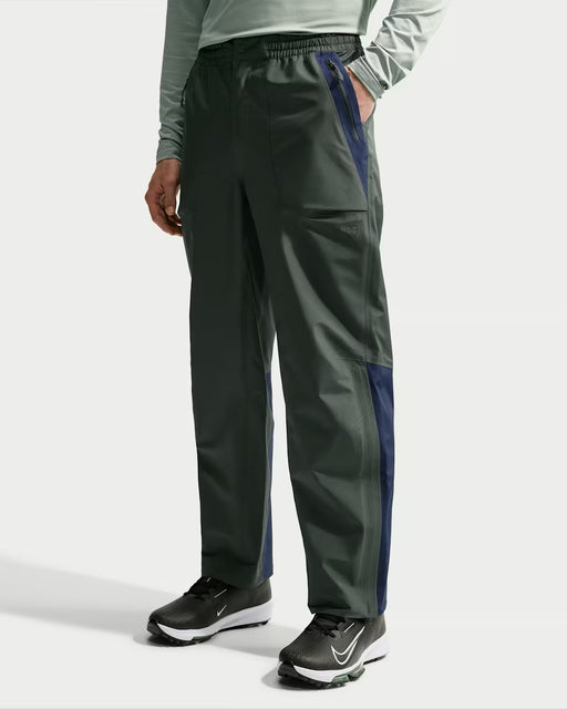 Nike Storm-FIT ADV waterproof golf trousers in camo green and navy, featuring a front view with zipped side pockets.