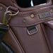 Close-up of brown leather Titleist LINKSLEGEND golf bag featuring antique brass hardware and branded metal plaque.