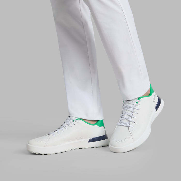 G/FORE G.112 Embossed Skull & Tees Spikeless Golf Shoes in white with green and navy accents on a model with his left heel off the ground