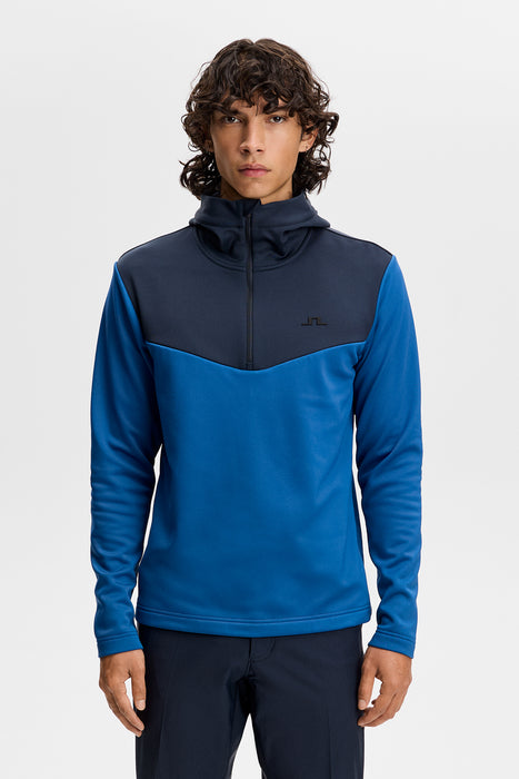 J.Lindeberg Maclean quarter zip golf hoodie in blue and navy with a high collar and hood, front view.