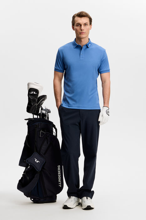 J.Lindeberg KV Print Golf Polo Shirt in federal blue on model standing next to golf bag