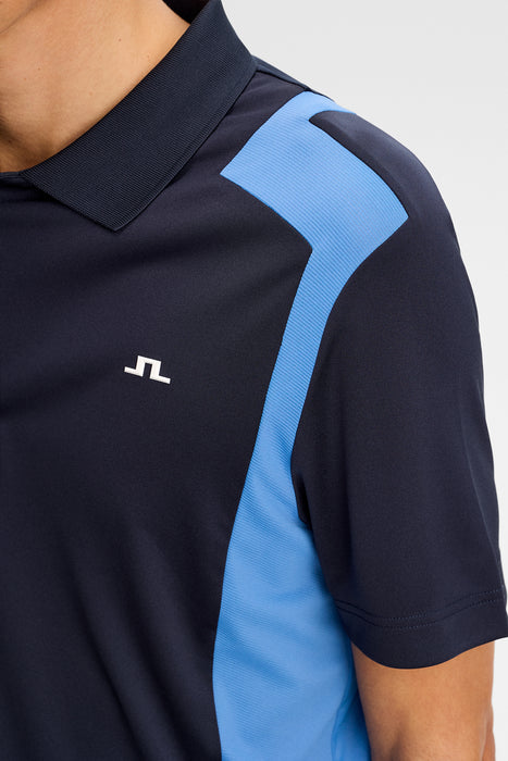 J.Lindeberg Legacy Golf Polo Shirt in navy with whit and blue. On model, close up of logo