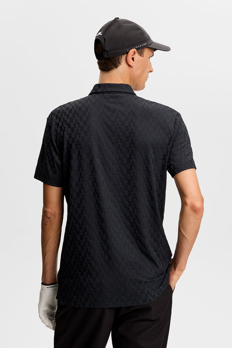 J.Lindeberg Kofe Golf Polo Shirt in black, showing full front of the polo in black on a model wearing a hat showing back of shirt