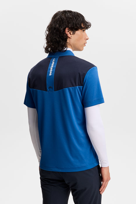 Back view of J.Lindeberg Calex golf polo in blue and navy with a vertical white logo stripe on the upper back.