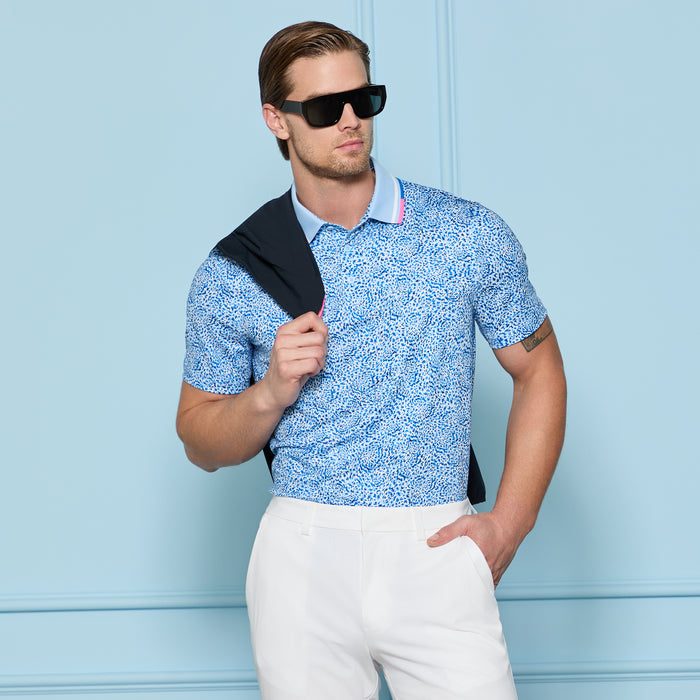 G/FORE Fireworks Tech Jersey Golf Polo Shirt in baja blue, on a model wearing sunglasses and holding sweatshirt