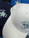 PING Fore Get Me Not golf hats in white, navy and blue with embroidered flower detail and PING branding.