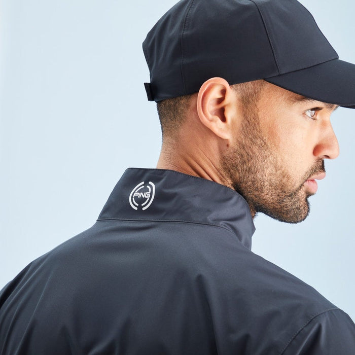 Man wearing a black jacket with a logo on the collar against a light blue background