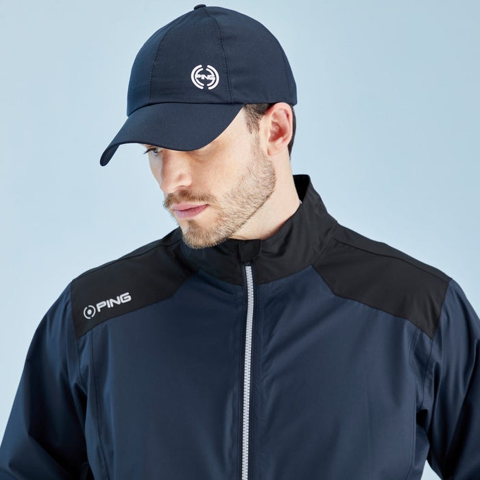 Front view of a navy and black PING AquaDrive waterproof golf jacket with a matching navy cap on a male model.