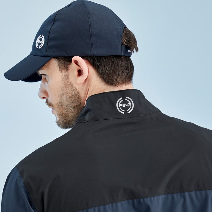 Rear view of a man wearing a black PING AquaDrive waterproof golf jacket and matching navy cap with logo detail.
