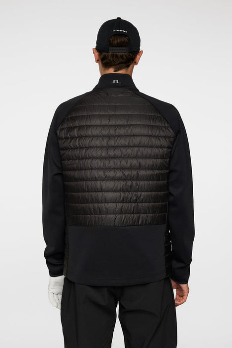 Person wearing a black quilted jacket and cap on a white background
