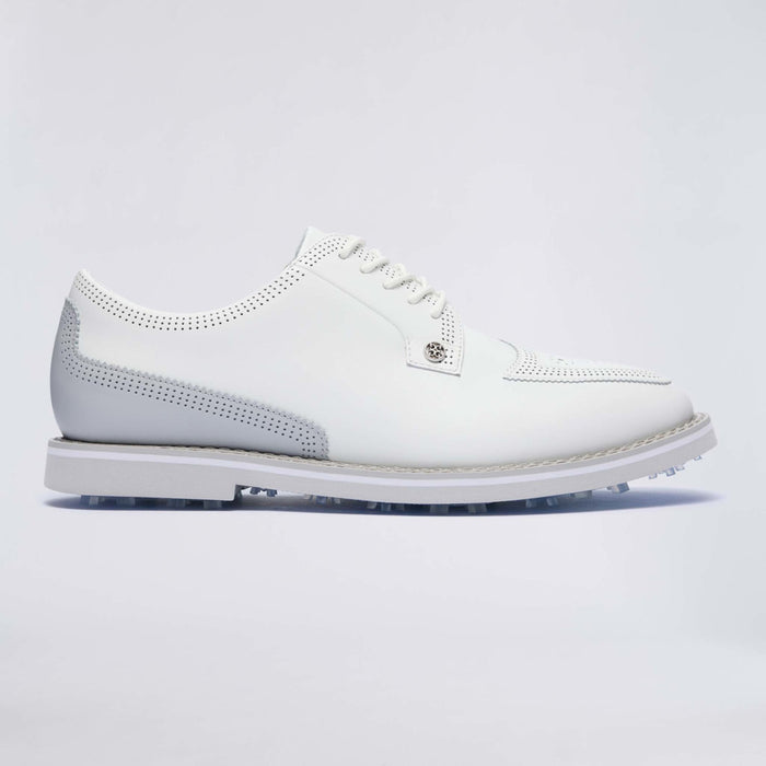 A white leather G/FORE Gallivanter Leather Brogue Men's Spikeless Golf Shoes with perforated details, a small silver-tone logo badge on the side, and a white sole with visible golf club tips, shown against a light grey studio background.