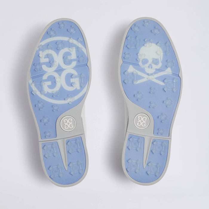 A pair of light blue and grey rubber soles shown from above, featuring a white GG logo on the left sole and a white skull and crossbones on the right sole, with the GG monogram also visible near the heel on the G/FORE Gallivanter Leather Brogue Men's Spikeless Golf Shoes