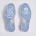 A pair of light blue and grey rubber soles shown from above, featuring a white GG logo on the left sole and a white skull and crossbones on the right sole, with the GG monogram also visible near the heel on the G/FORE Gallivanter Leather Brogue Men's Spikeless Golf Shoes