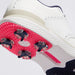 Close-up of a white G/FORE Gallivan2R Brogue Saddle Men's Golf Shoes showing the textured white upper, beige midsole, and bright pink sole with dark navy golf spikes.