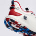 A close-up of a high-top G/FORE MG4+ O2 Perforated Men's Spikeless Golf Shoes in white, red, and navy blue, showing the textured side panel, red heel overlay, navy pull tabs, and a patterned sole with spikes in red, white, and navy.