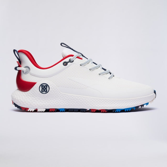 A white G/FORE MG4+ O2 Perforated Men's Spikeless Golf Shoes with red and blue accents, featuring a textured white upper, white midsole, red heel tab, and a black circular logo on the side, set against a light grey background.