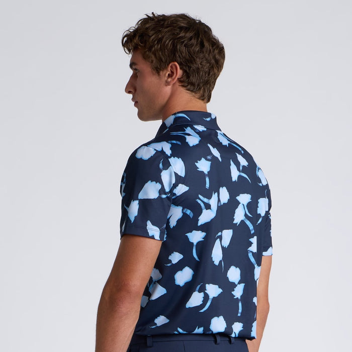 Man wearing a navy blue G/FORE Ghost Floral Tech Jersey Men's Golf Polo Shirt with light blue floral pattern on a plain background