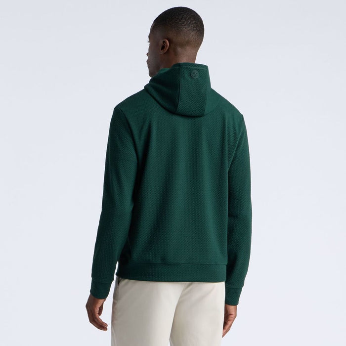 A man viewed from the back wearing a dark green G/FORE Pebble Quilted Men's Golf Hoodie and light beige pants, set against a plain light grey studio background.