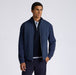 A man wearing a navy blue G/FORE Storm Fleece Hybrid Men's Golf Jacket over a dark sweater and collared shirt, standing against a light grey studio background.