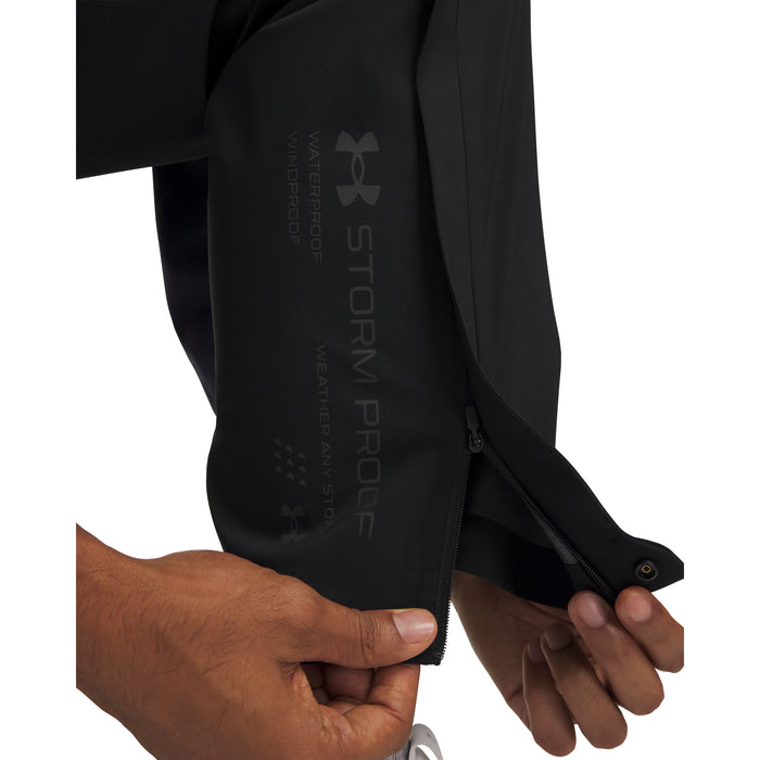 Close-up of black Under Armour Drive Pro waterproof golf trousers showing the zipped leg hem and Storm Proof branding.